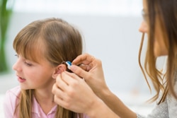 Hearing Aid Specialist Fitting Hearing Aid On Child