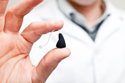 Hearing Instrument Specialist Holding Up A Hearing Aid