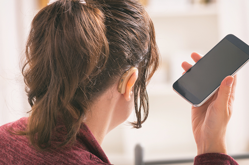 Woman Connecting Wireless Hearing Aids To Smart Phone