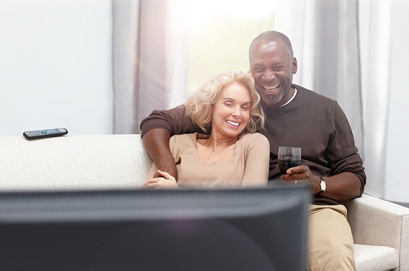 Loving Couple Enjoying Watching TV With Wireless Hearing Aids