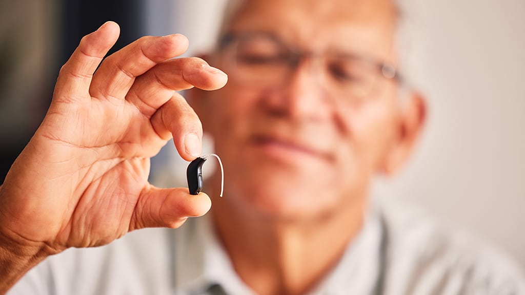 Senior man holding a hearing aid during a hearing aid maintenance appointment at Bravo Hearing Centre in Mississauga, representing support for age-related hearing loss.