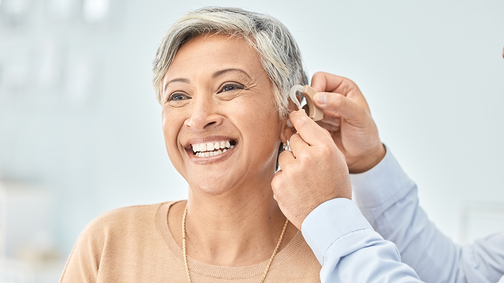 Smiling woman receiving hearing aid maintenance from a hearing specialist at Bravo Hearing Centre in Mississauga, representing personalized hearing care for adults.