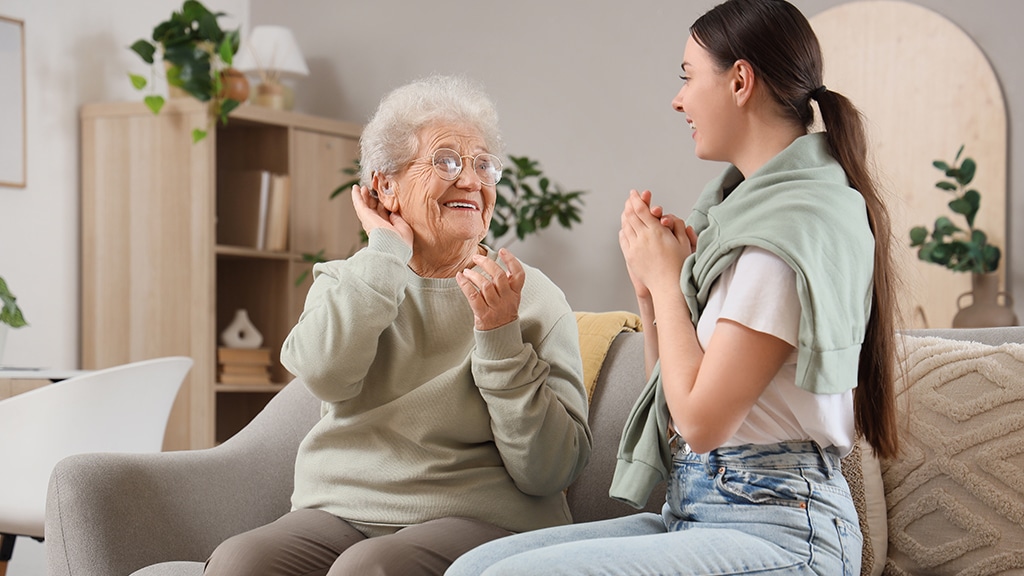 Senior woman smiling with her hearing aids while speaking with her daughter at home, representing the impact of hearing aid maintenance for families in Etobicoke and Mississauga.